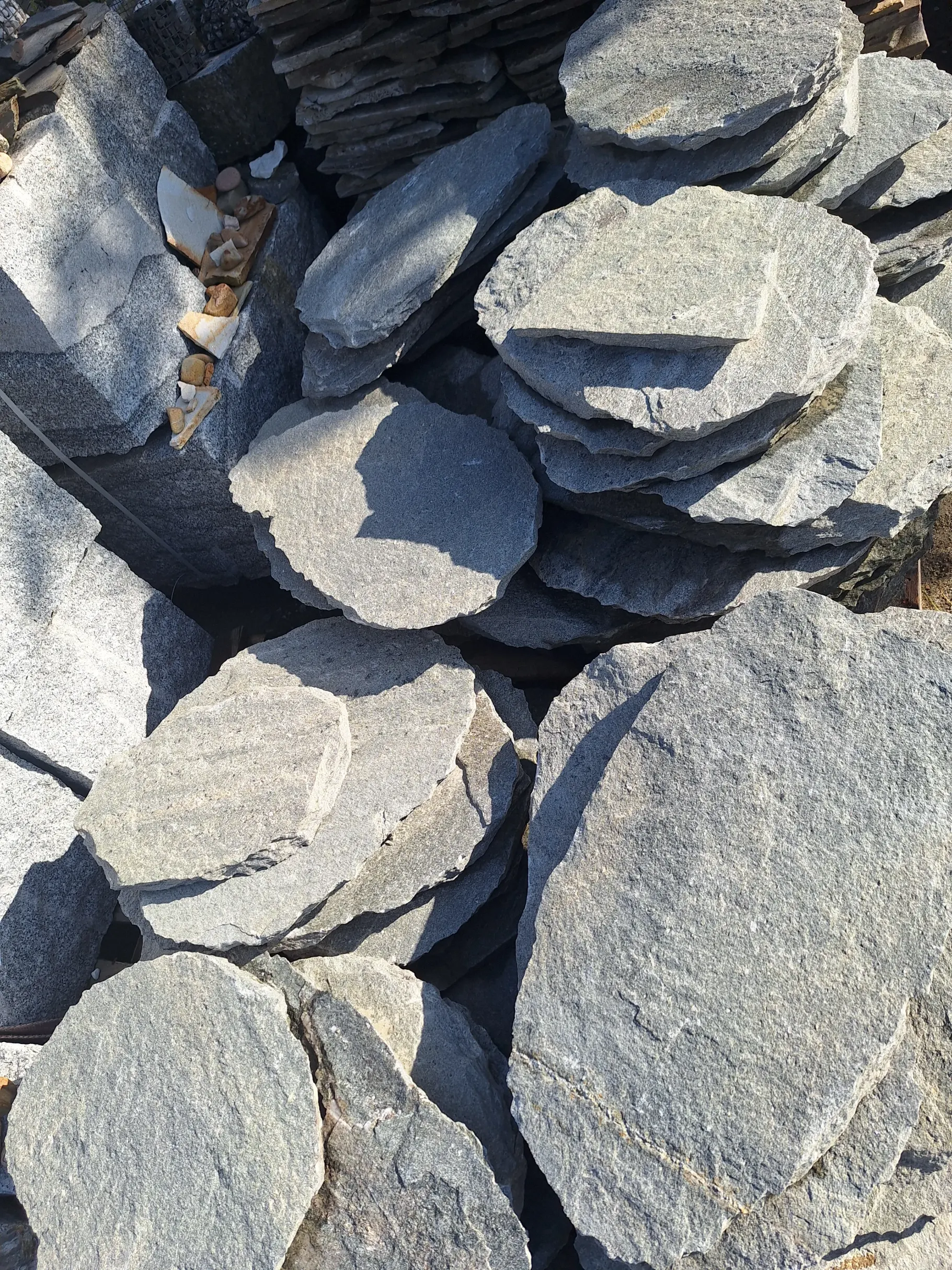 Stosy nieregularnych, okrągłych płyt bazaltowych przygotowanych do układania