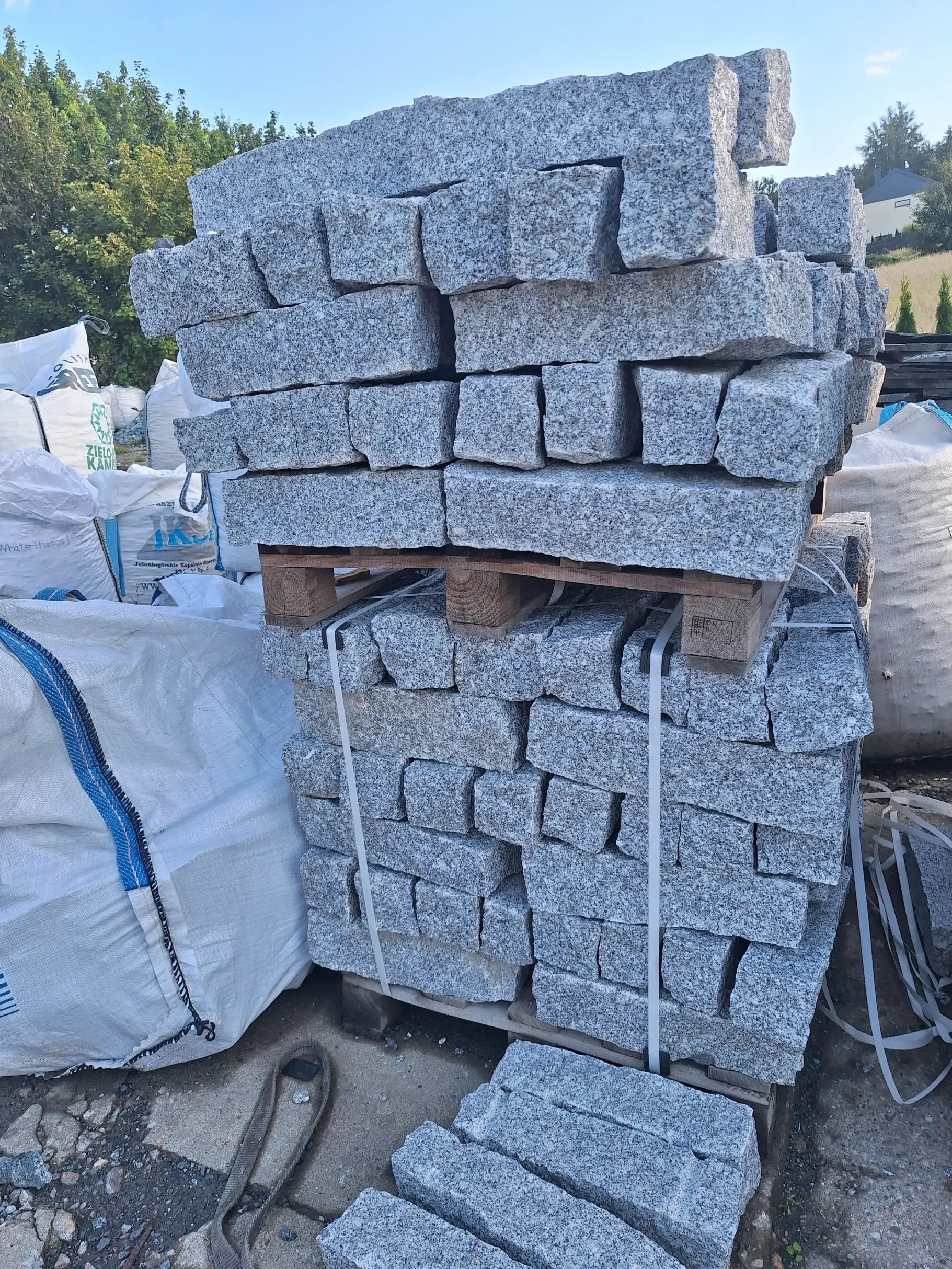 Stos szarych granitoidów – surowych, prostokątnych bloków kamiennych na palecie do montażu