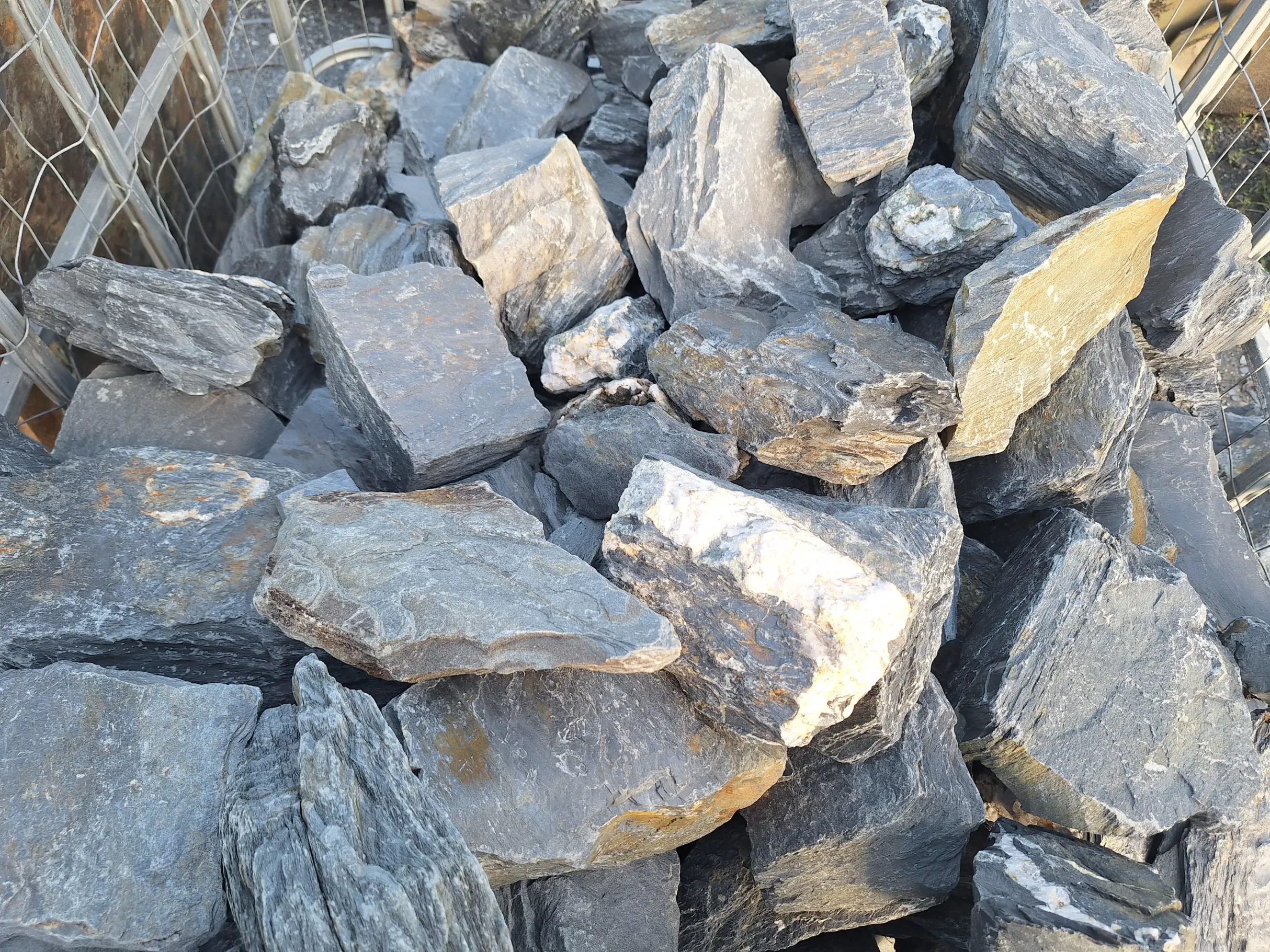 Sterta płaskich szarych kamieni do gabionów (grys) o nieregularnych kształtach w metalowym koszu