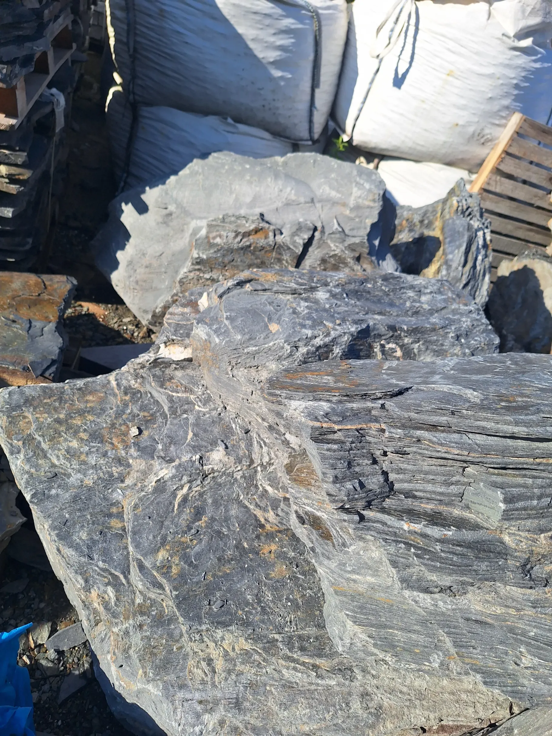 Stos dużych, płaskich, łupanych płyt skalnych o szarofalistej fakturze