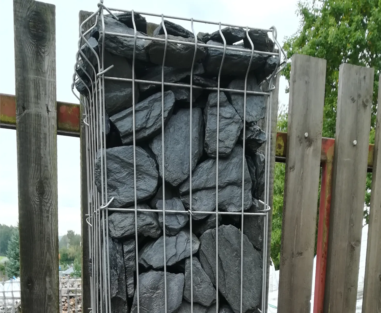 Metalowy kosz gabionowy z nieregularnymi czarnymi kamieniami bazaltu